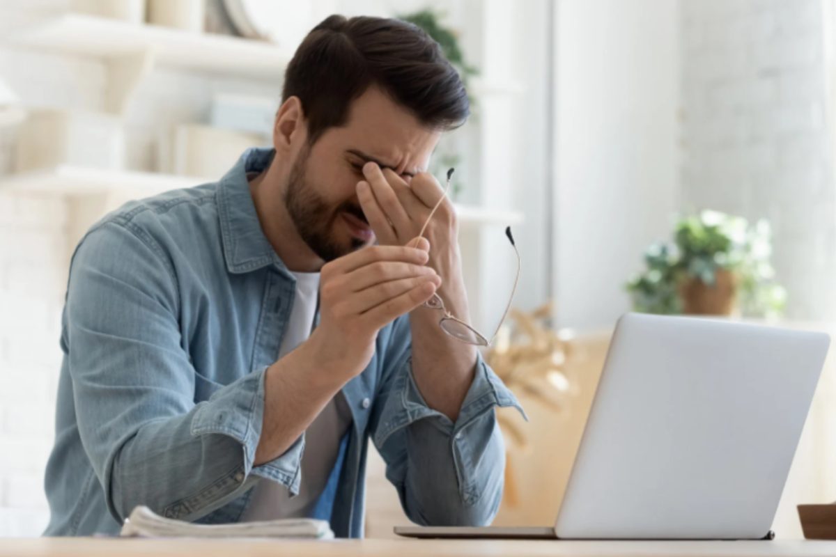 uomo stanco seduto davanti al computer che si tocca gli occhi