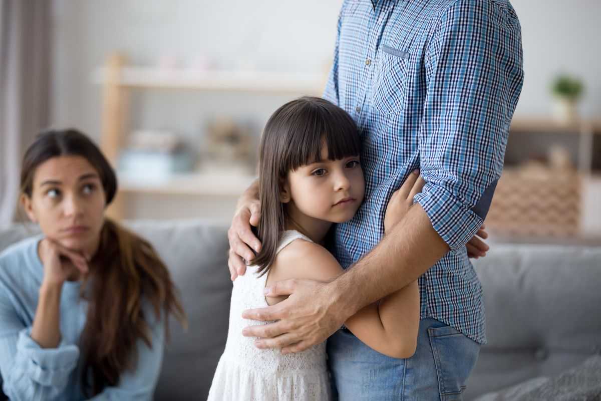 figlia abbraccia padre e madre guarda da lontano