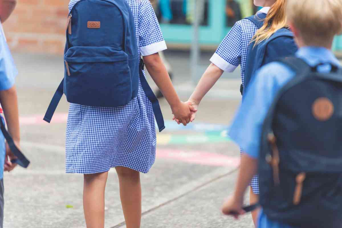 Due bambine con gli zaini e grembiule che si tengono per mano