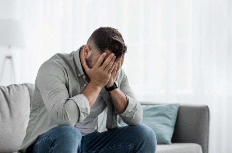 uomo disperato seduto sul divano con le mani in faccia